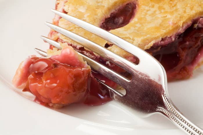 A fork cutting into a slice of cherry pie