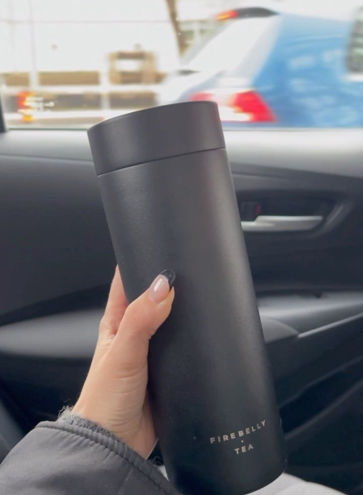 a person holding the firebelly steeping mug in their car
