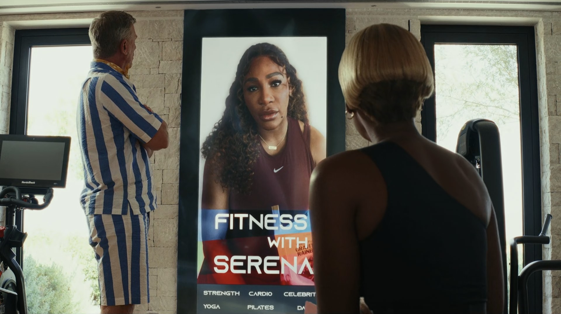 Serena Williams speaks on a screen while Janelle Monáe and Daniel Craig look at her