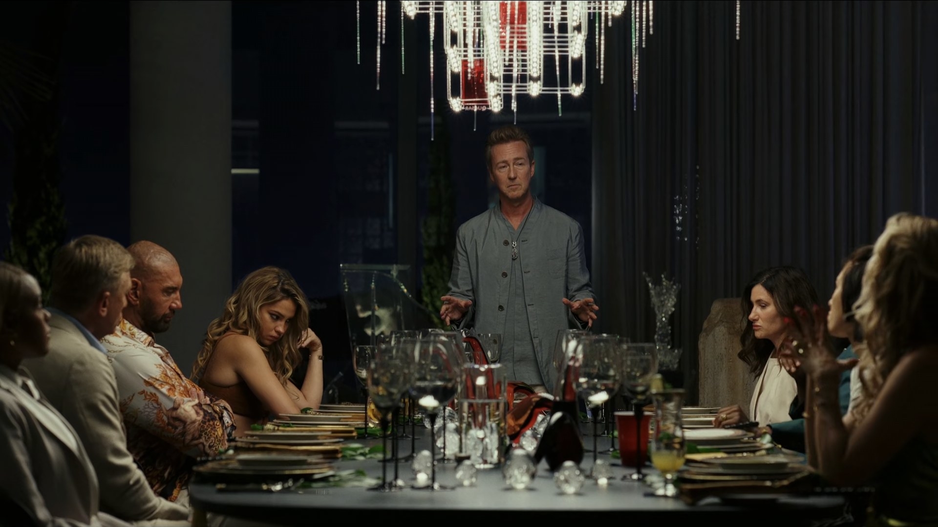 Edward Norton talks to his guests as they are sitting around a dining table