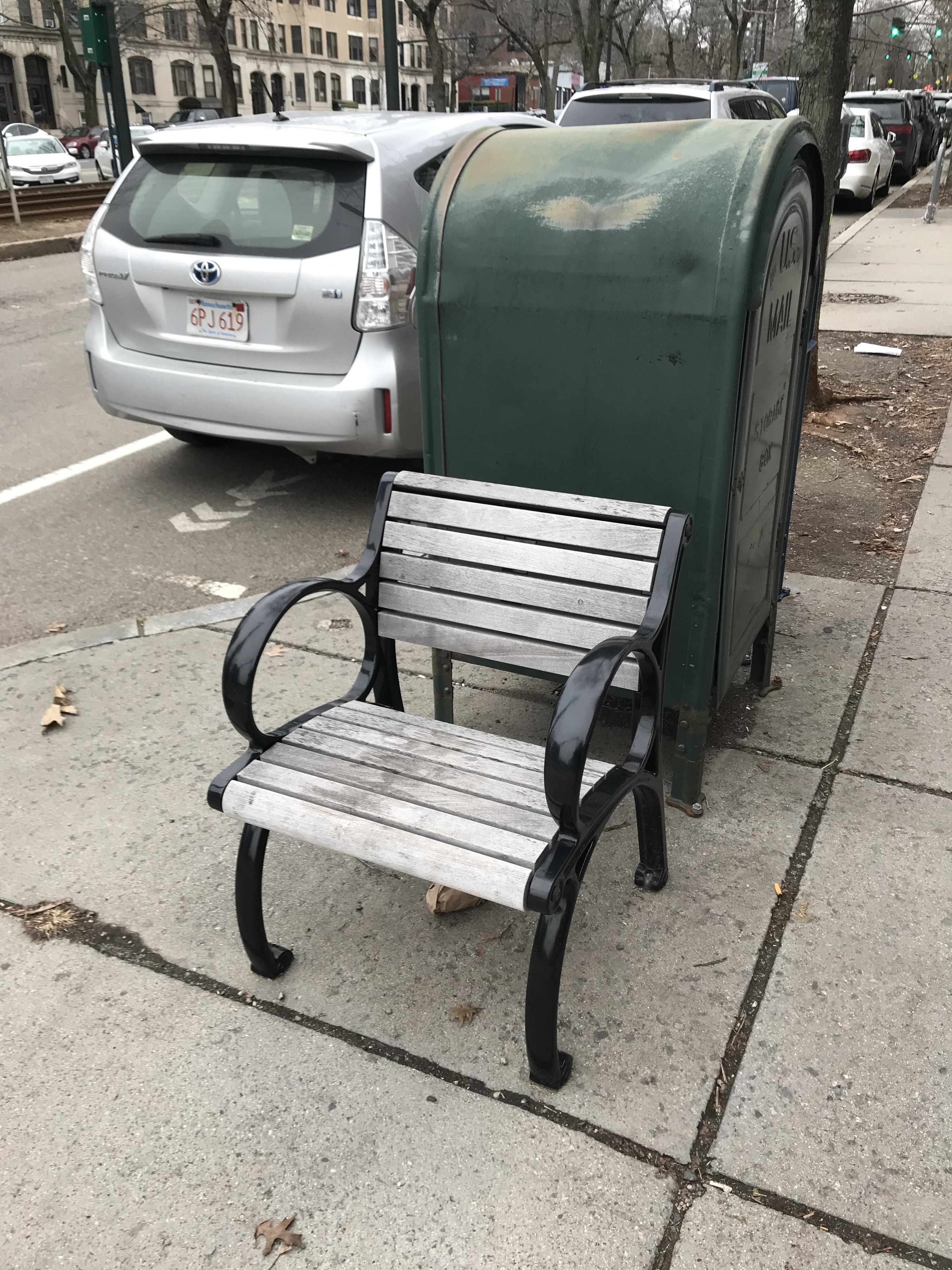 A narrow bench next to a mailbox on a city street