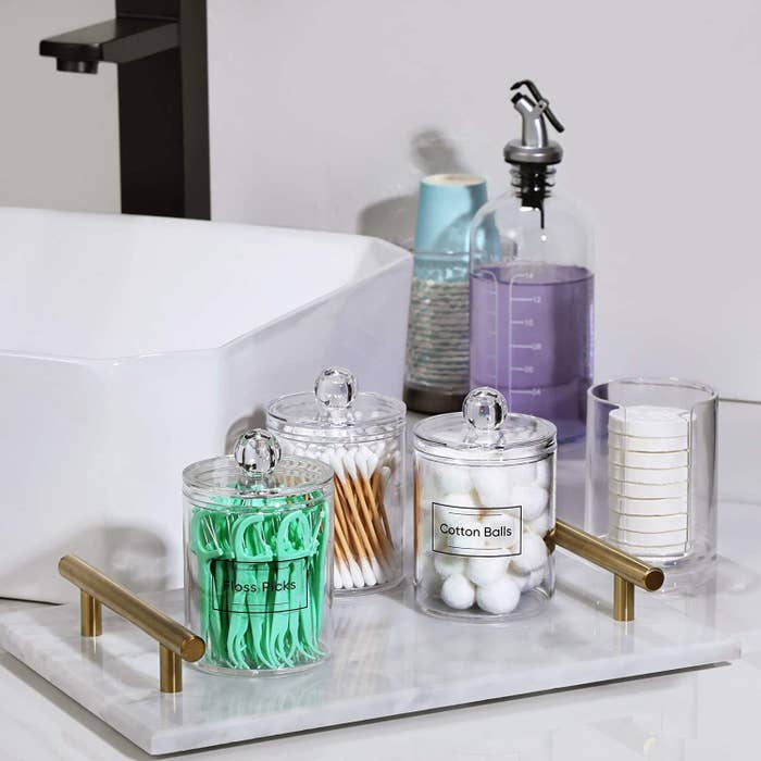 the containers on a tray in a bathroom with flossers, cotton swabs, cotton balls and soap