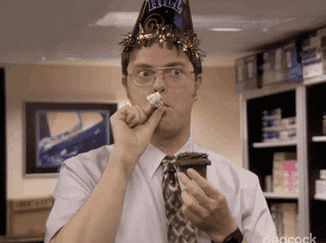 gif of dwight from the office holding a cupcake with a birthday hat on. andy smiles and gets into the shot.