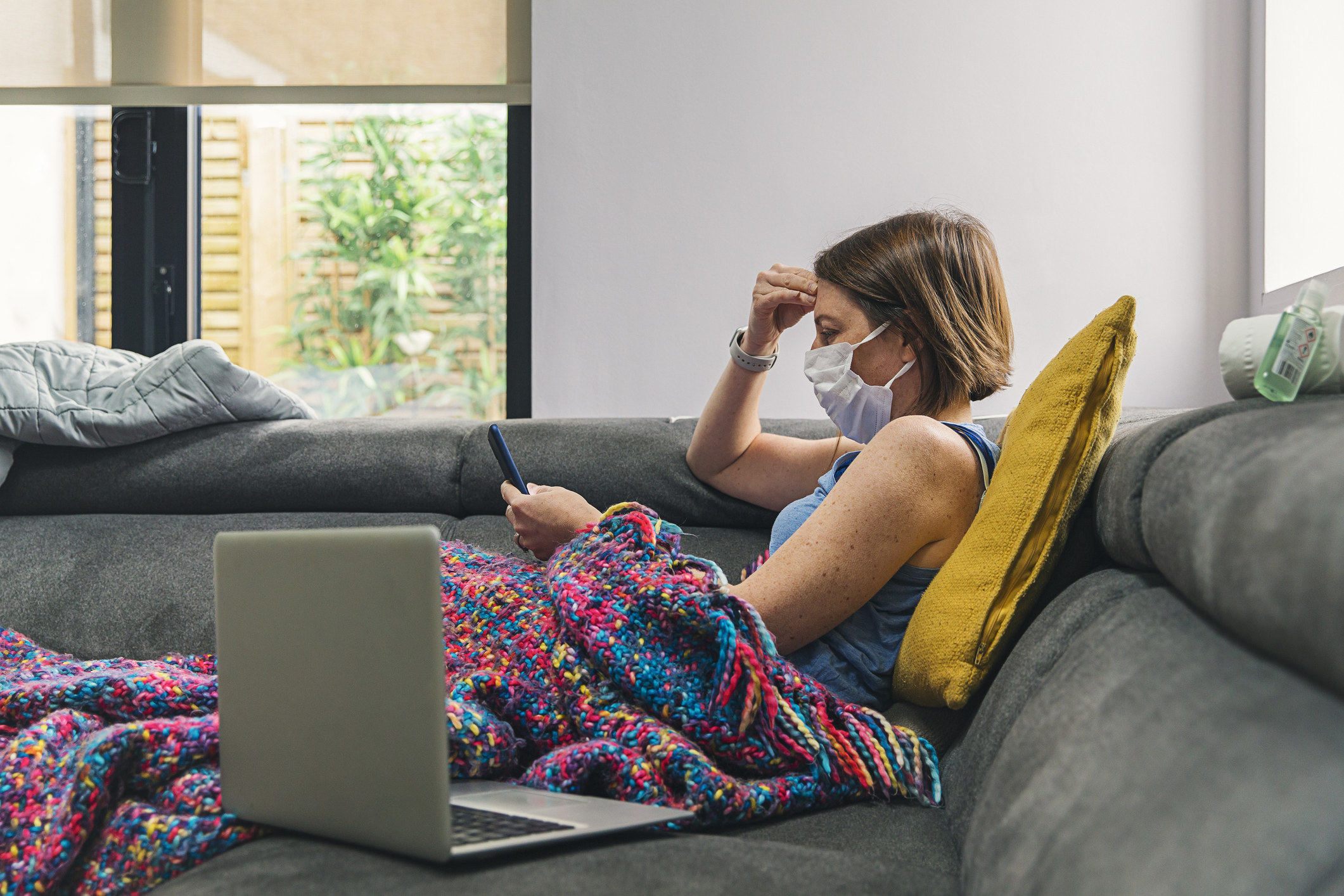 person self-isolating on a couch with a face mask