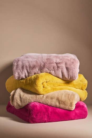 a stack of blankets, one pale pink, one marigold, one tan, and one hot pink