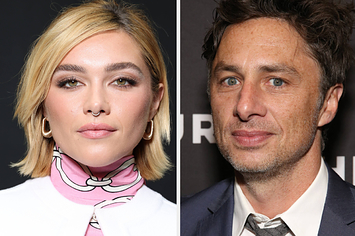 Florence Pugh wears a pink turtleneck sweater with white designs under a white blazer with gold hoop earrings. Zach Braff wears a blue suit with a gray tie.