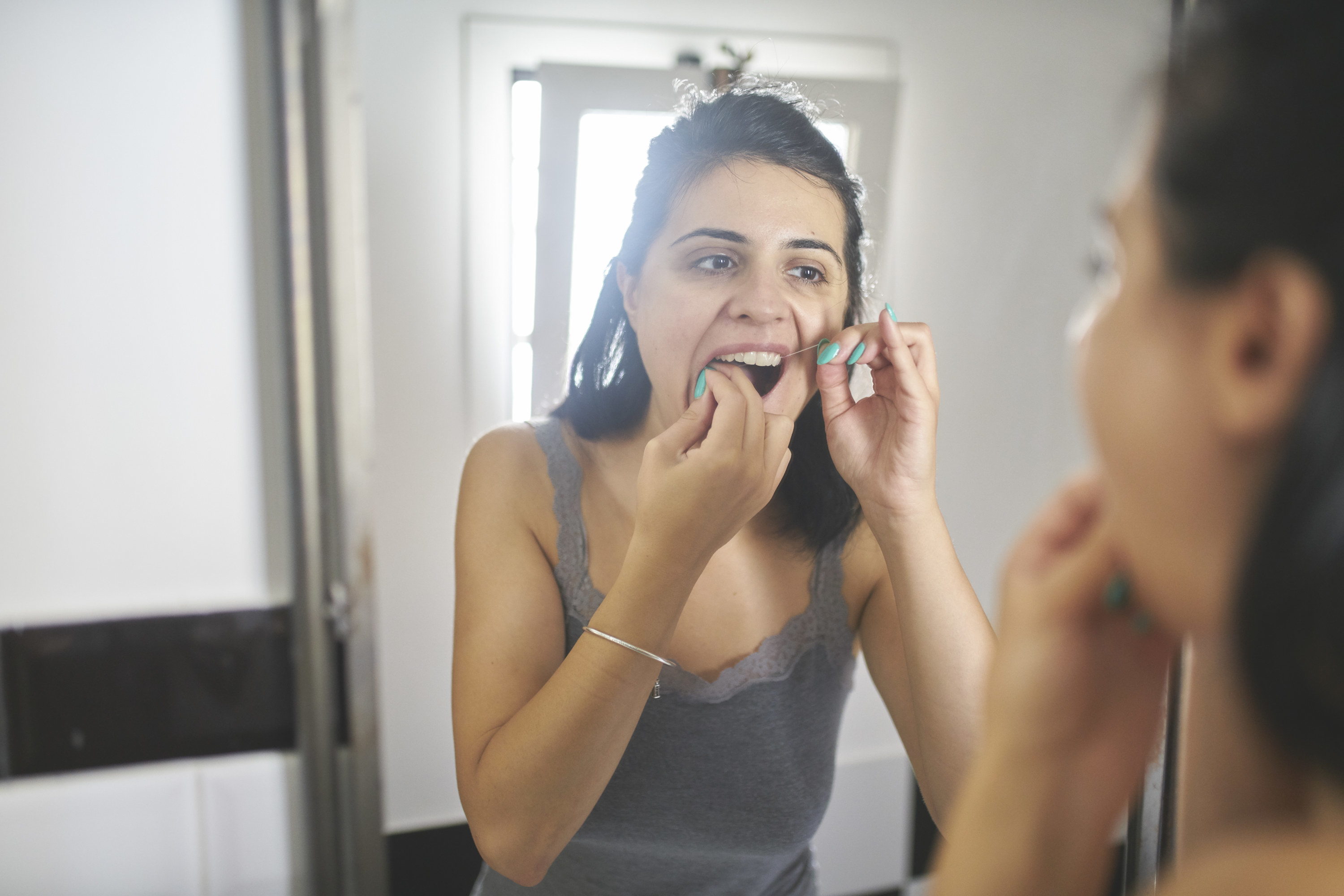 a woman flossing her teeth in a bathroom mirror