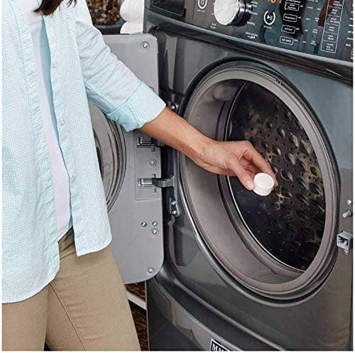a person putting a washing machine cleaner tablet into a washing machine