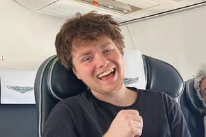 alex warren sits on a plane and laughs with all teeth showing