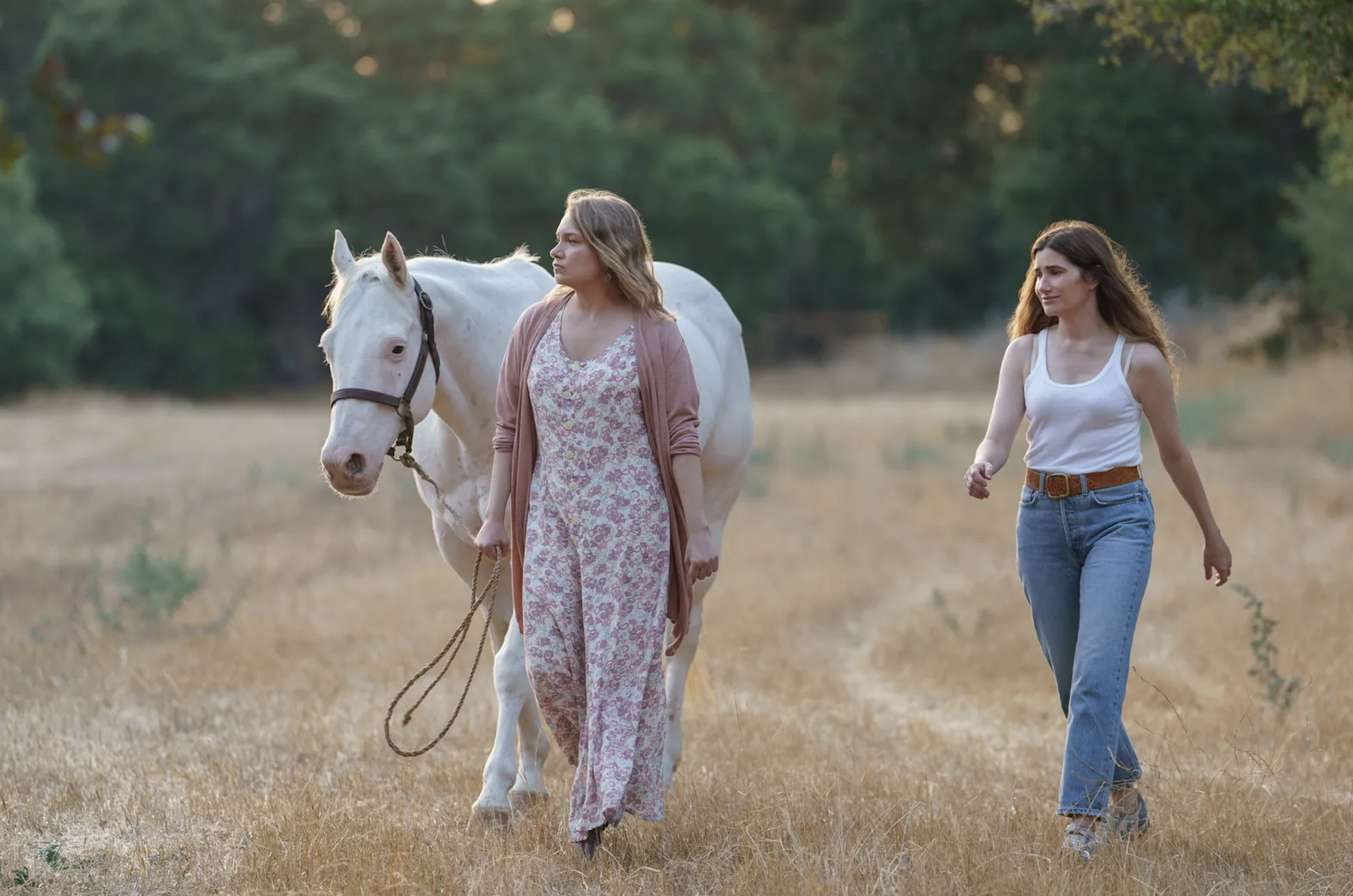 two woman walking in the fields with a horse
