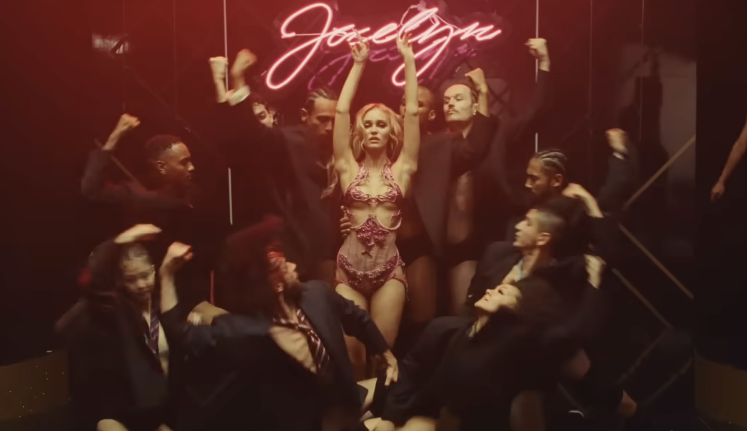 woman dancing under a neon sign reading Jocelyn with dancers in suits surrounding her