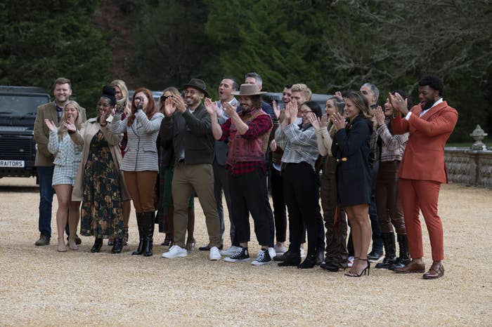 The cast of Traitors stand clapping in a drive way