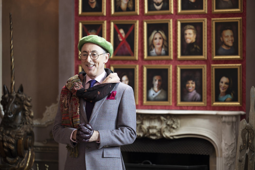 Alan Cumming stands in front of a wall of portraits