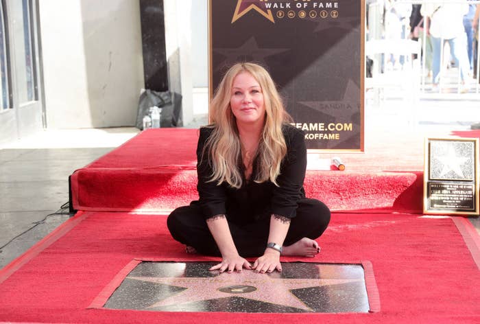 Christina sitting cross-legged in front of her star on the Hollywood Walk of Fame with her hands on the plaque