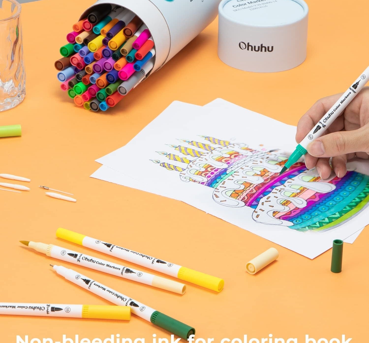 the markers on a table and someone using them to colour a photo of a birthday cake