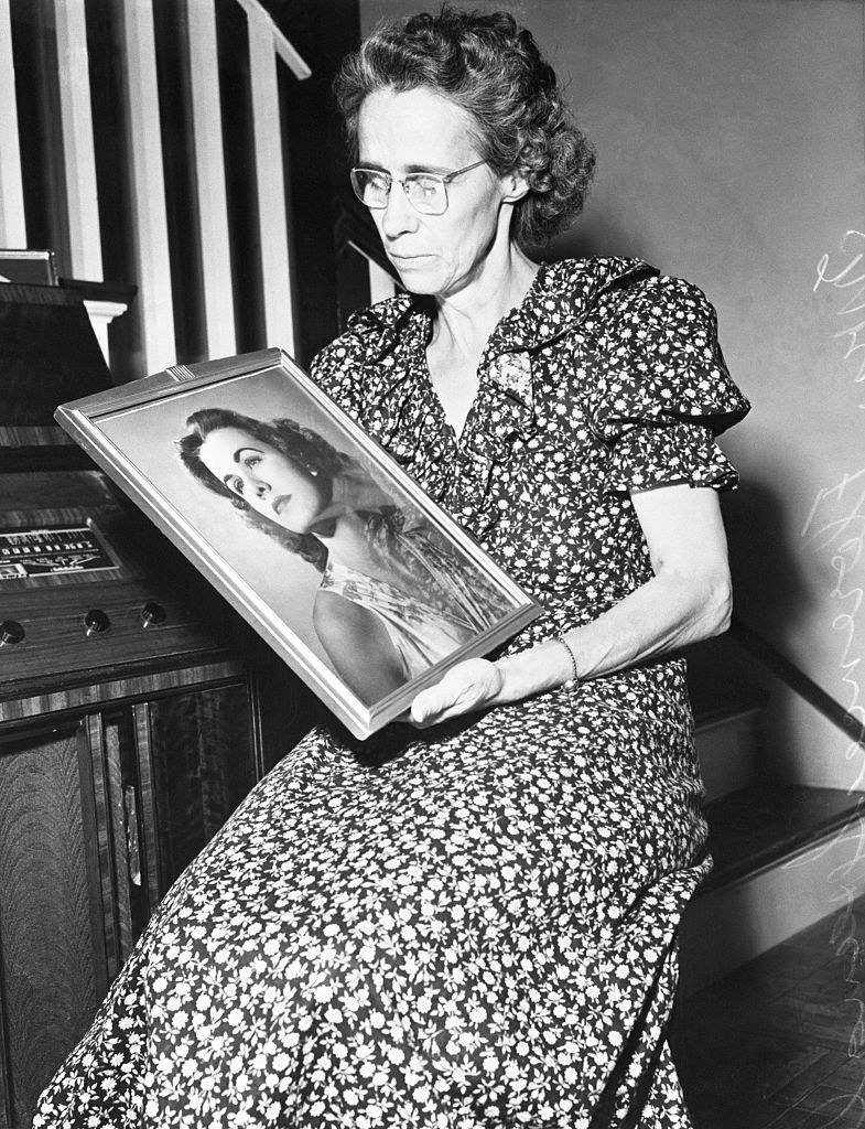 Black-and-white photo of a woman holding a painting of a woman