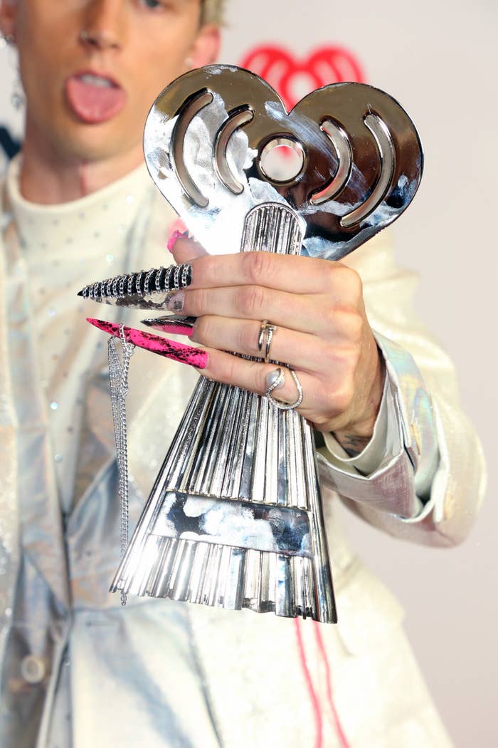 Machine Gun Kelly holds and award and shows off his extra long acrylic nails