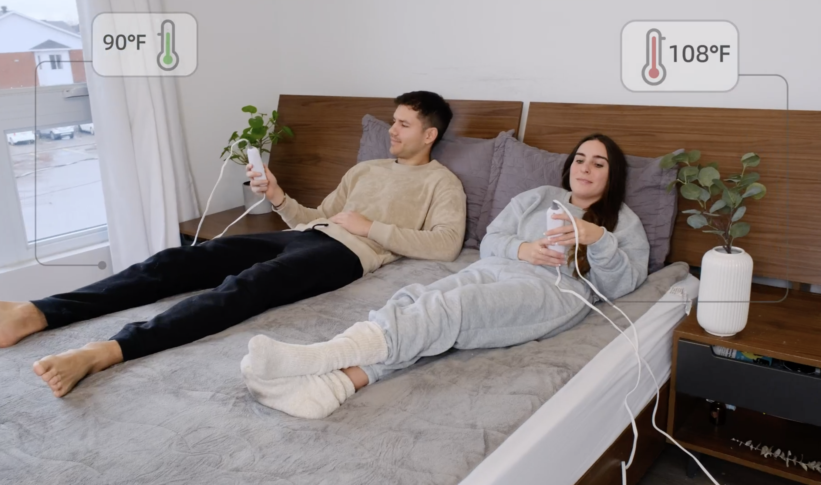 couple sitting on a bed with the heated mattress pad each adjusting their temperatures