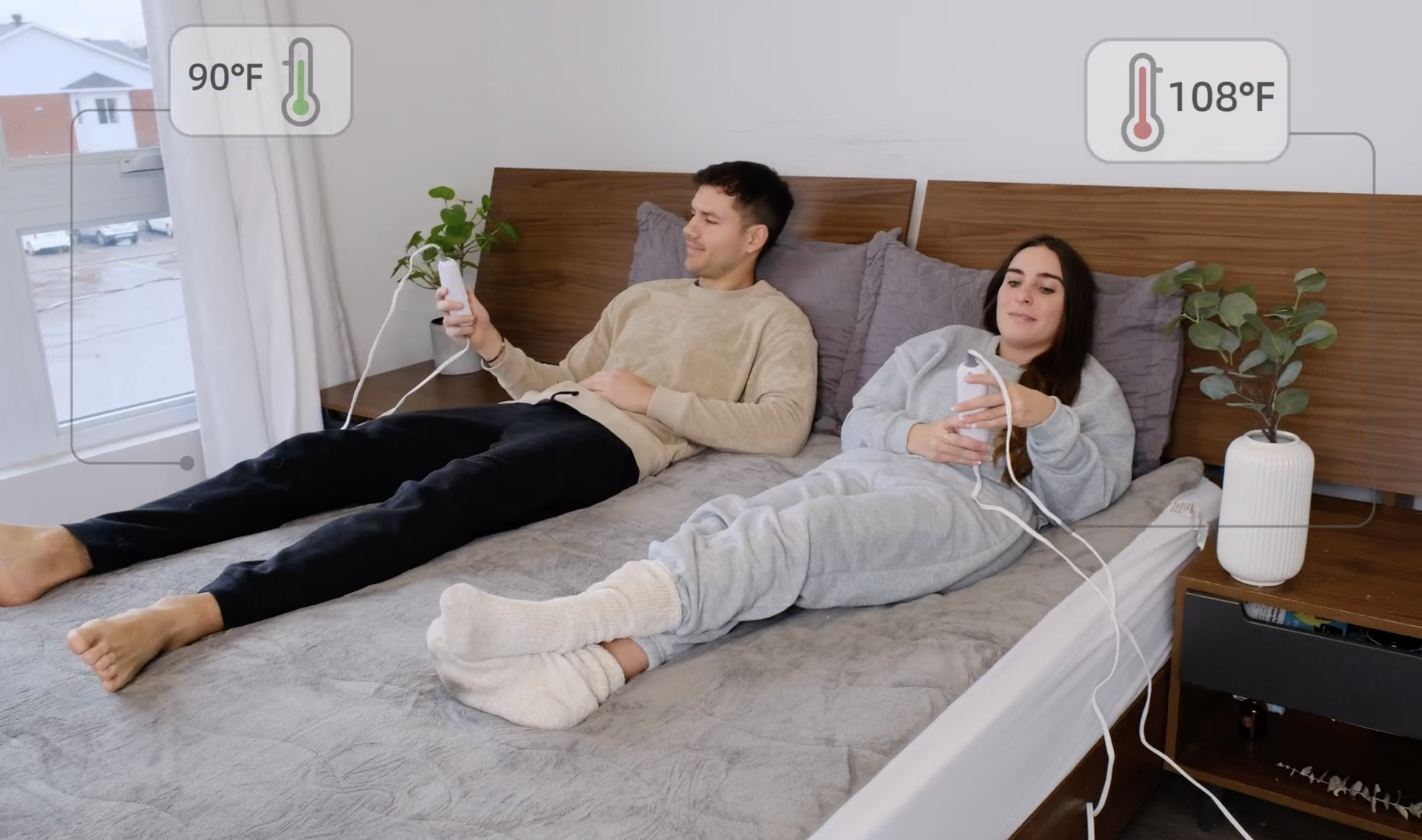 couple sitting on a bed with the heated mattress pad each adjusting their temperatures