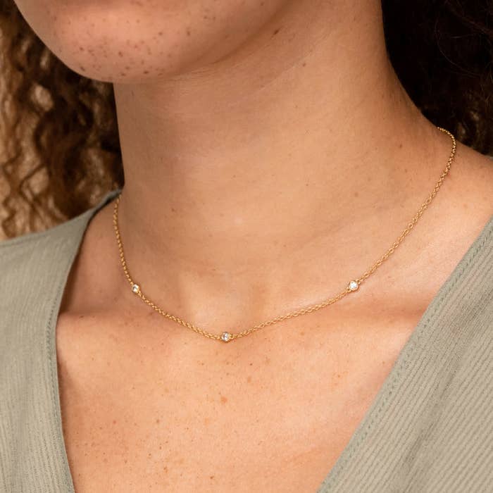 a person wearing a gold necklace with three shiny sapphires on it