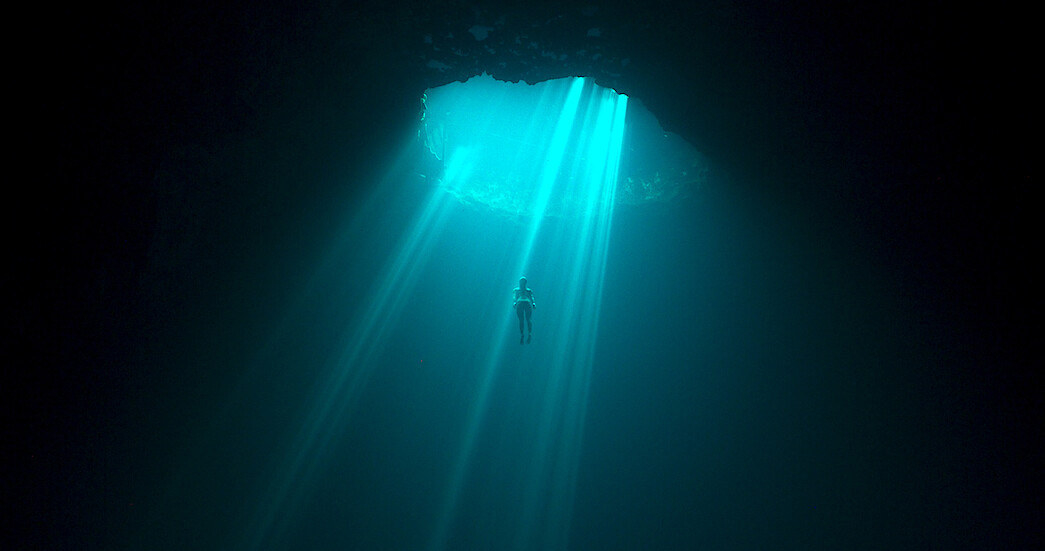 someone floating deep in a water sinkhole with light coming in through the opening
