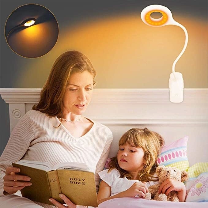 a parent and child in bed reading a book with the light clipped to the head board