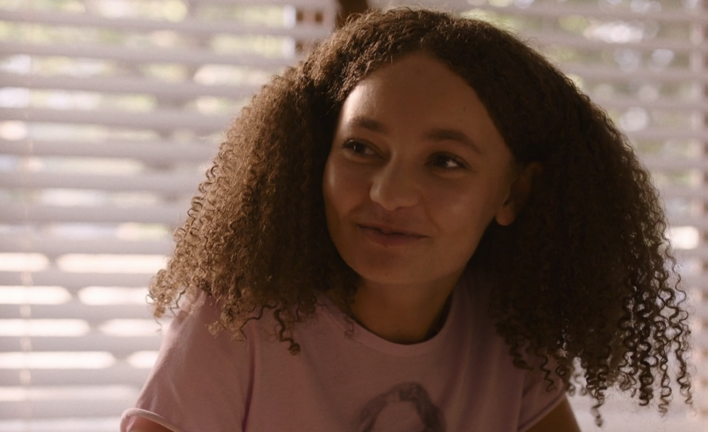 Joel&#x27;s daughter Sarah in the series smiling while she&#x27;s sitting in front of a window with blinds