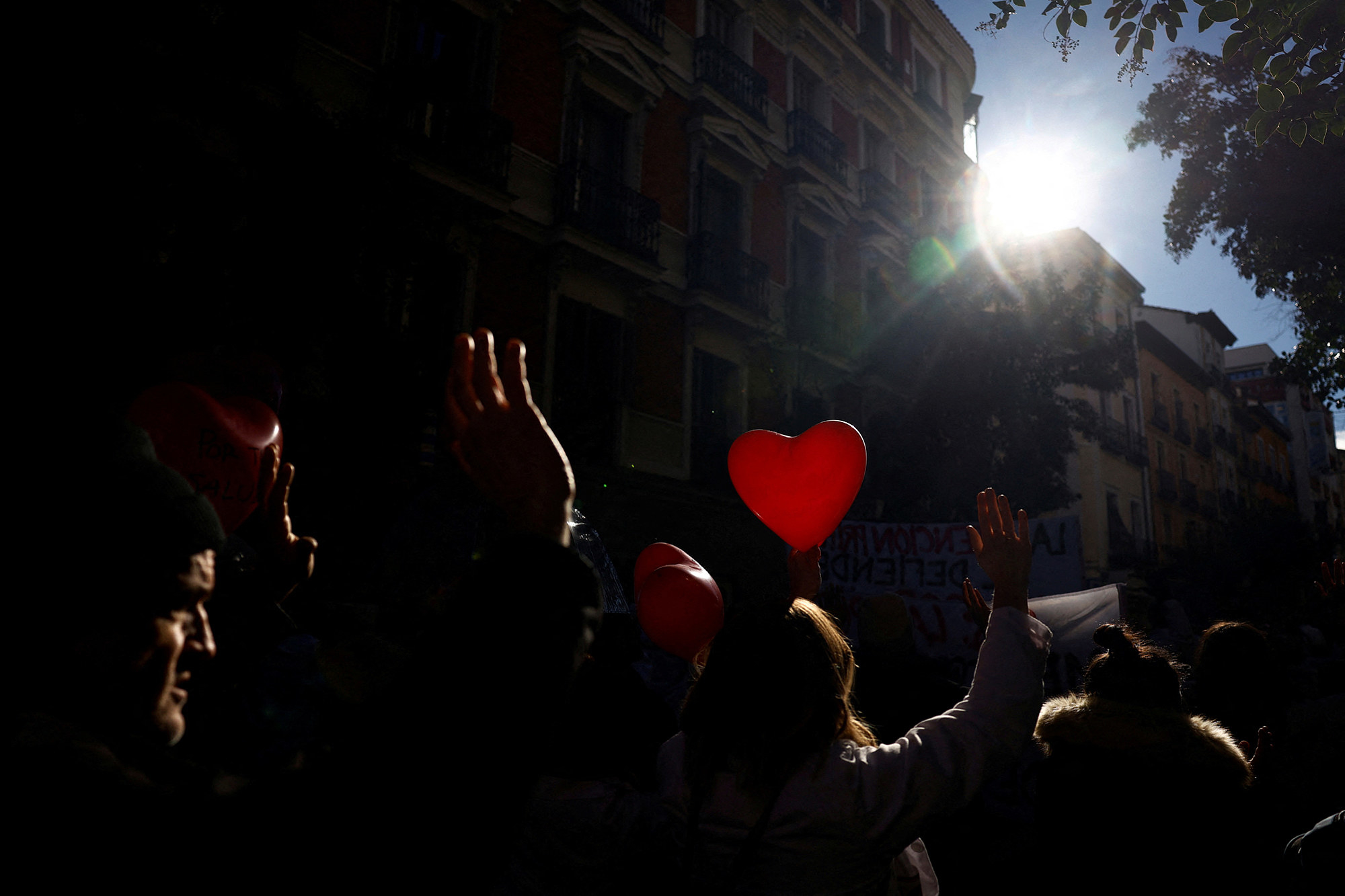 a crowd of people outside covered in shadows, a single red heart balloon glows