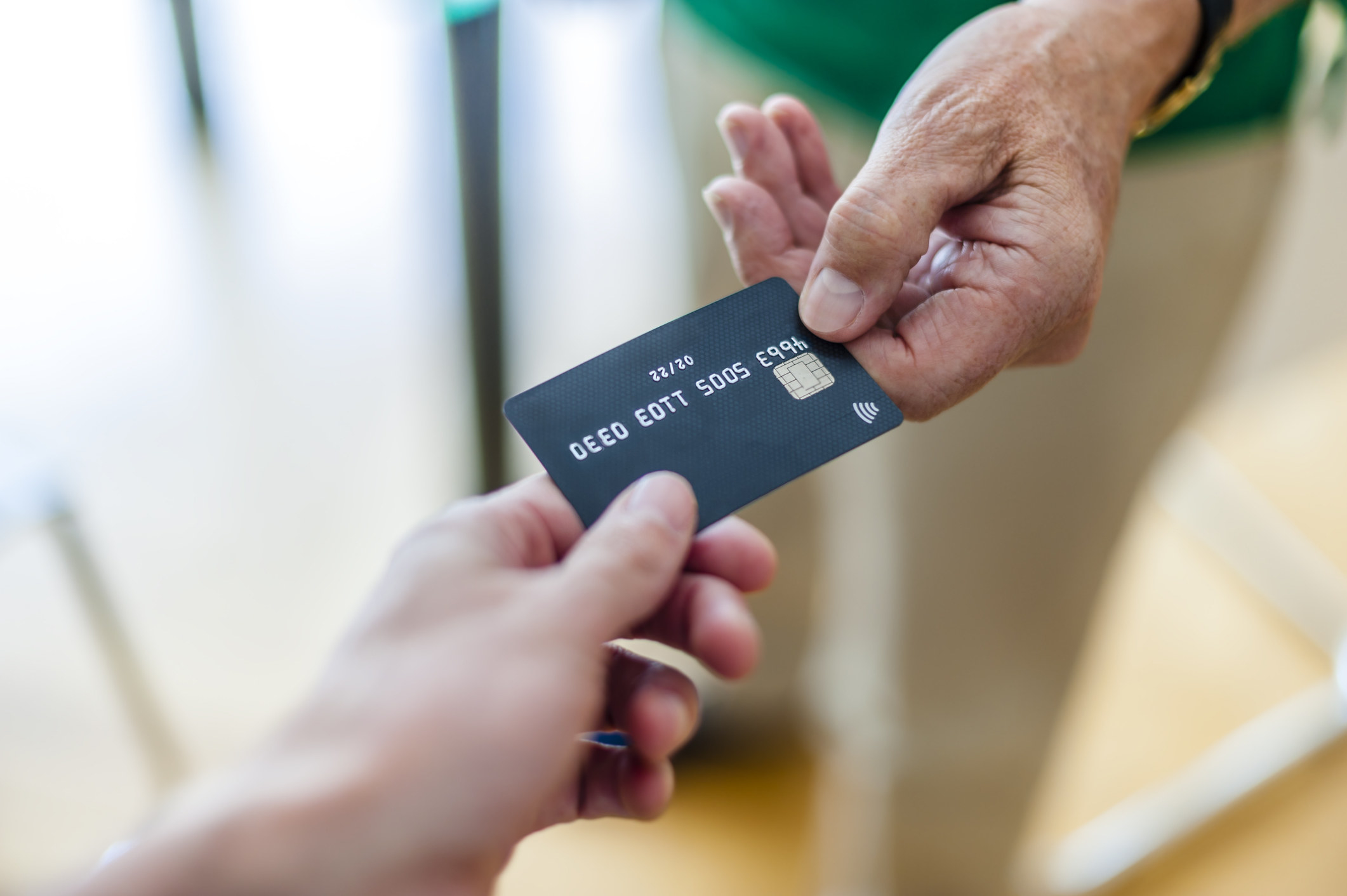 One person hands a credit card to another person&#x27;s outstretched hand