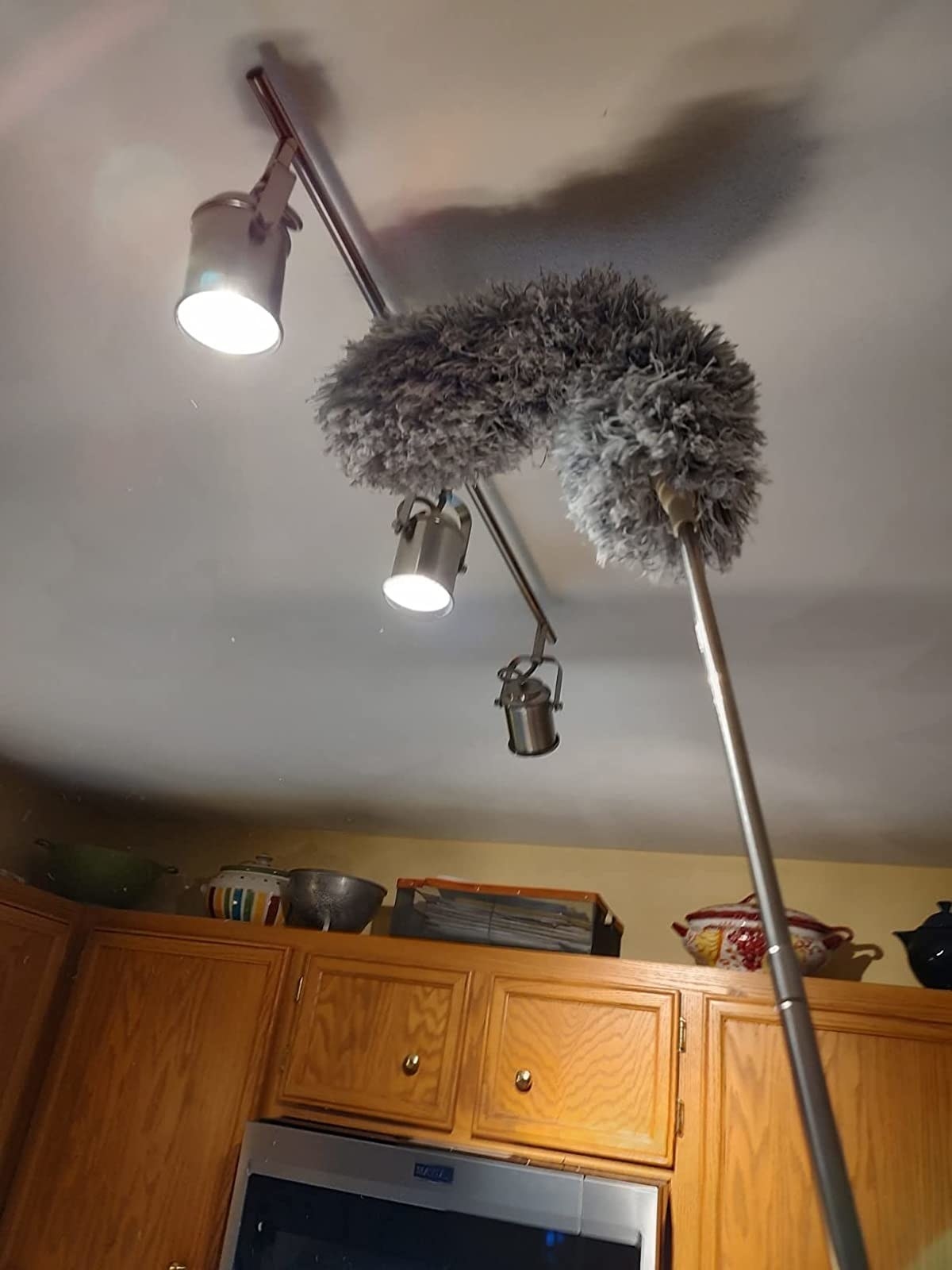 a reviewer photo of the grey duster being used to clean silver track lights in a kitchen
