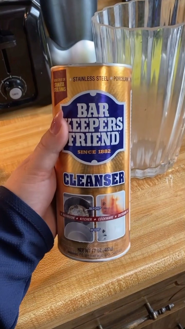 a person holding up a container of bar keepers friend cleansing powder