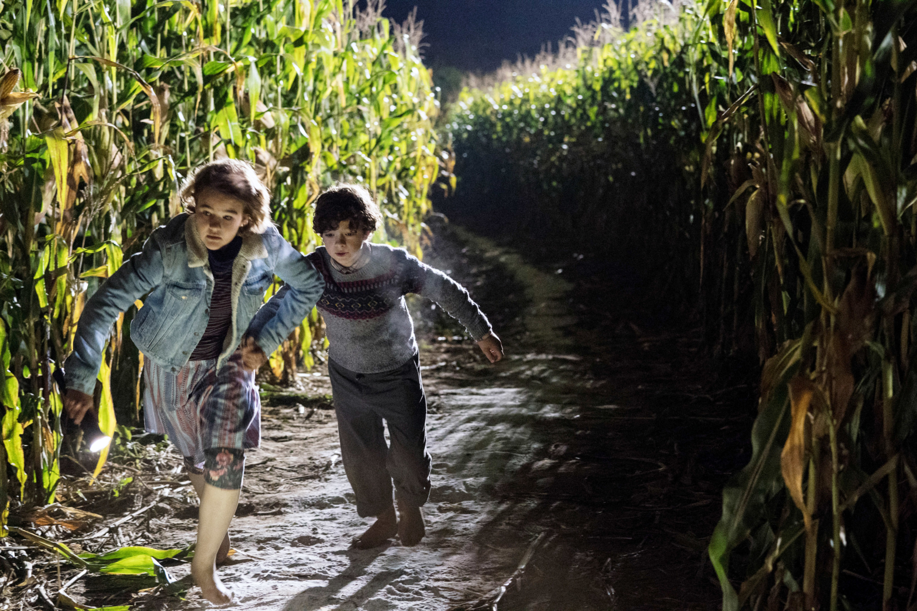 Two children run through a corn field