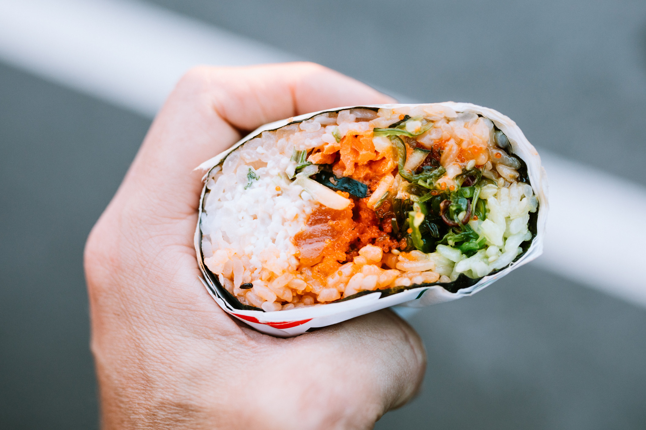 A sushi burrito in someone&#x27;s hand.