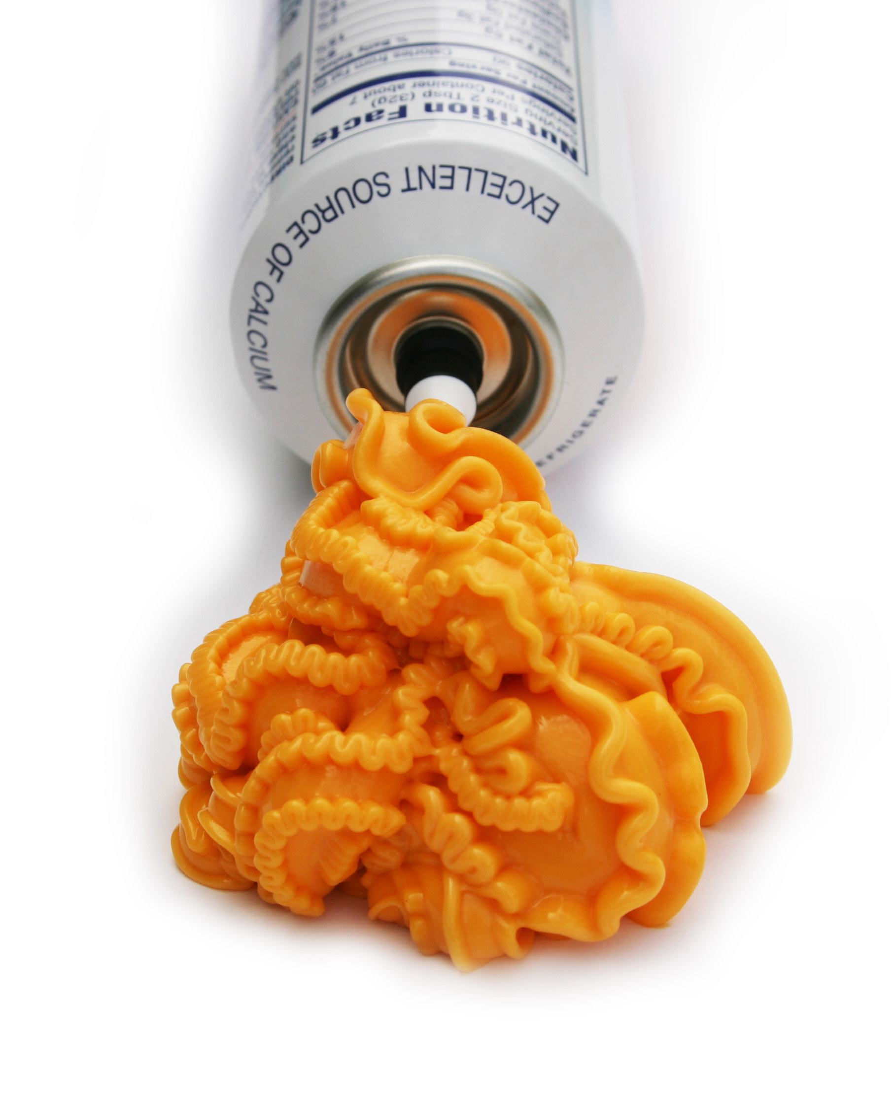 An opened tube of orange spray cheese with a large amount coming out, shaped intricately, against a white background