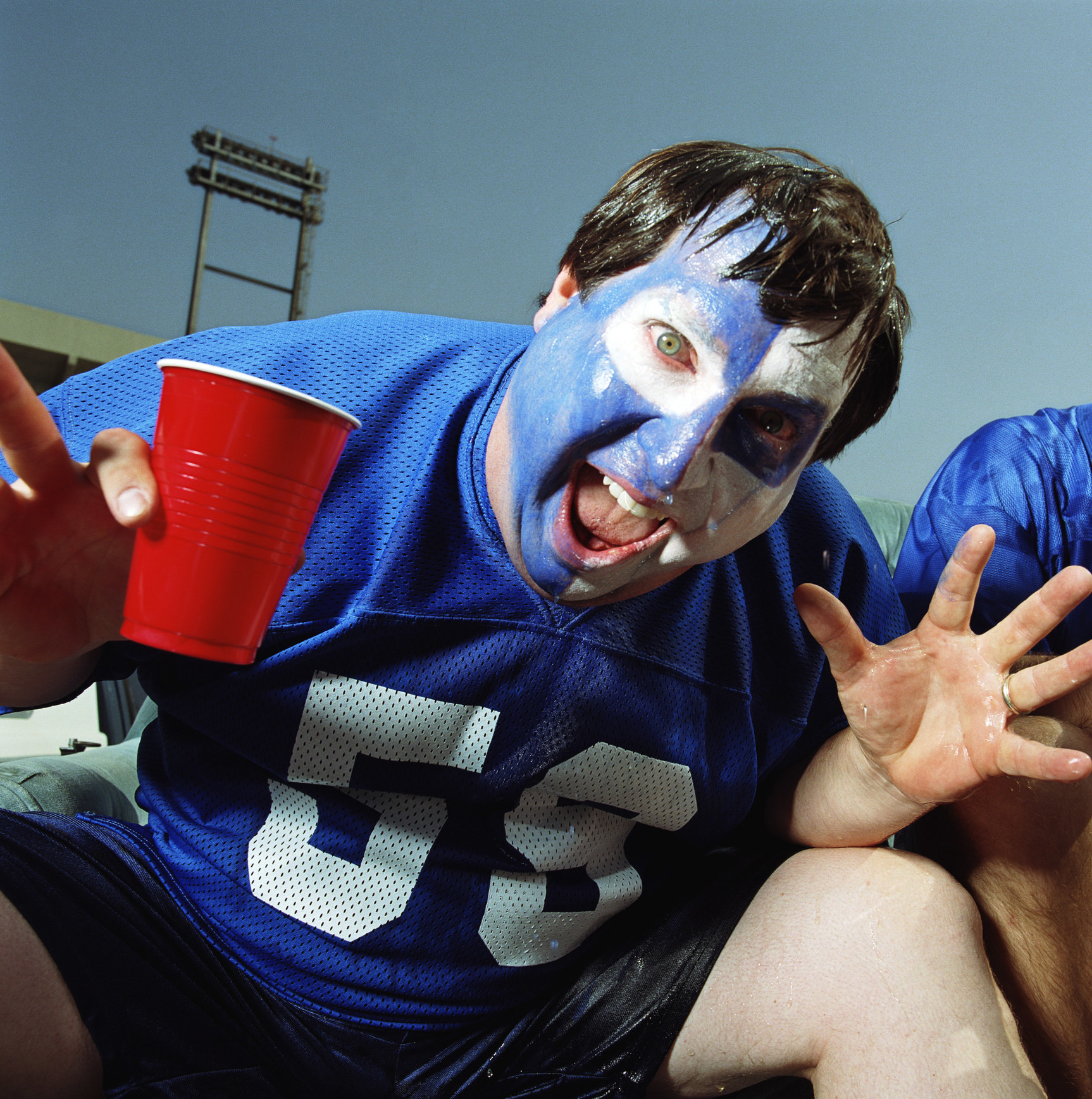 Sports fan with face paint and jersey and holding a red cup