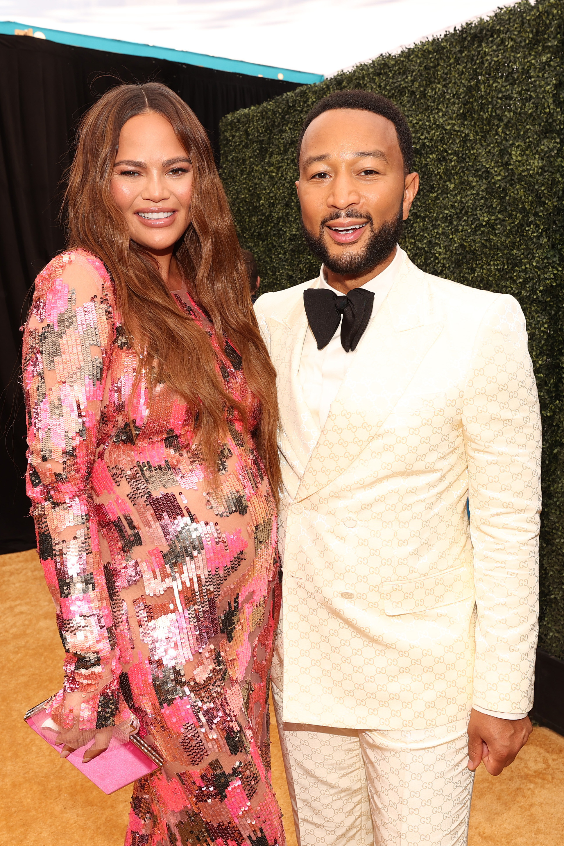 A pregnant Chrissy wears a sequined long-sleeved dress as she poses for a photo with John who&#x27;s wearing suit and bowtie