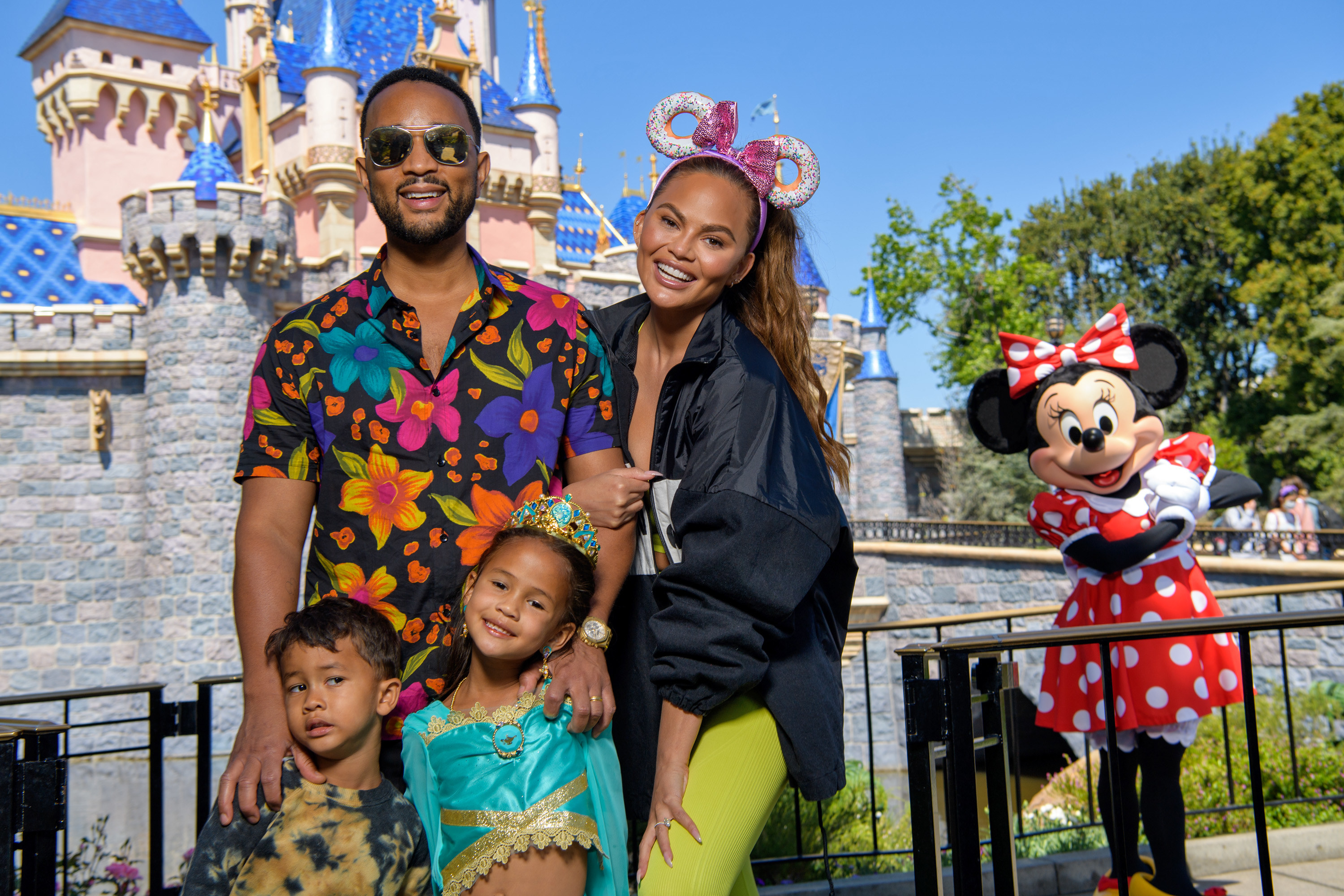 John, Chrissy, Luna, and Miles smile for a family photo at Disneyland with Minnie Mouse in the background