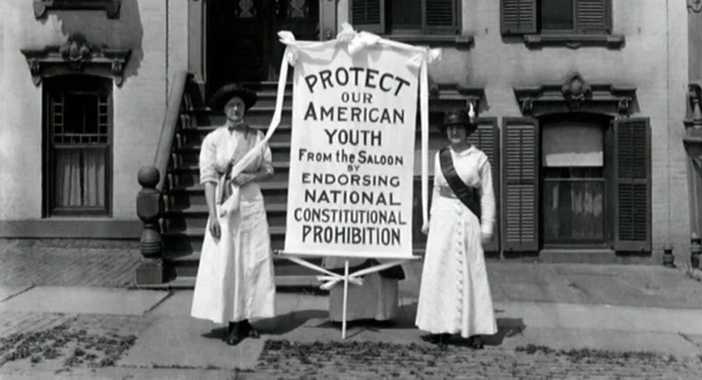 Two women standing in a street with a sign &quot;Protect our American youth from the saloon&quot;