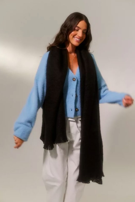Model wearing black blanket scarf, white pants and blue top