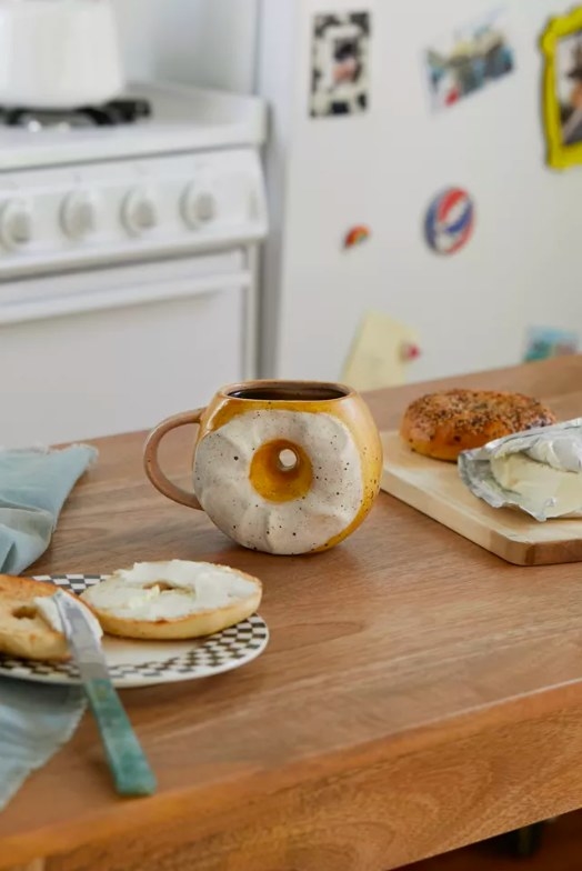 Bagel shaped mug next to a plate with a sliced bagel