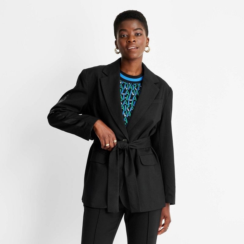 Model wearing black blazer over colorful top with black pants