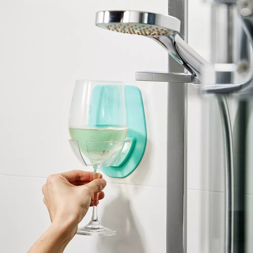 A hand placing a glass of white wine in the seafoam wine holder in the shower