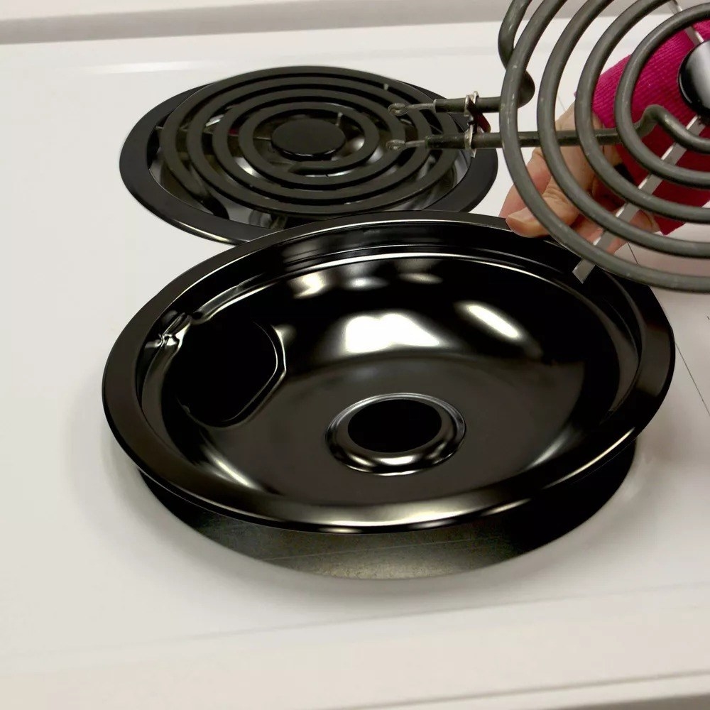 Someone placing the black drip pans on a white stovetop
