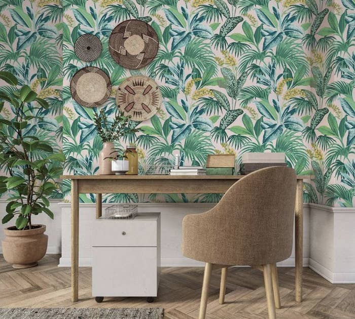 A desk and chair in front of botanical wall paper