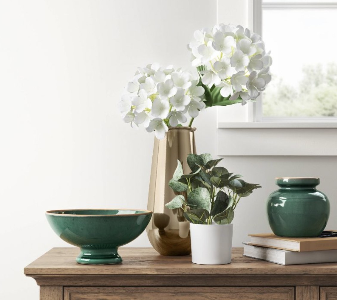 a fake eucalyptus sitting on a wooden dressed in front of a vase of white flowers