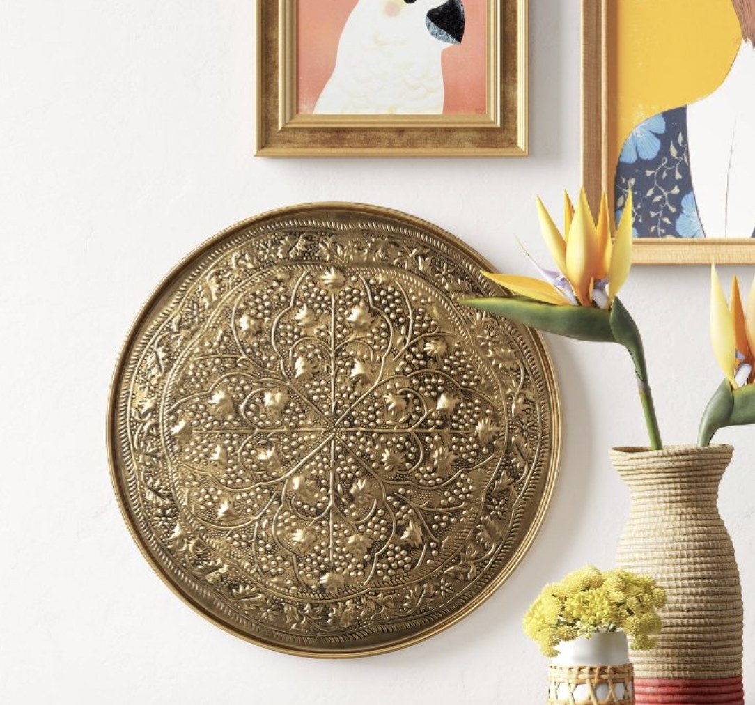 A gold medallion wall-hanging on a white wall next to a woven vase