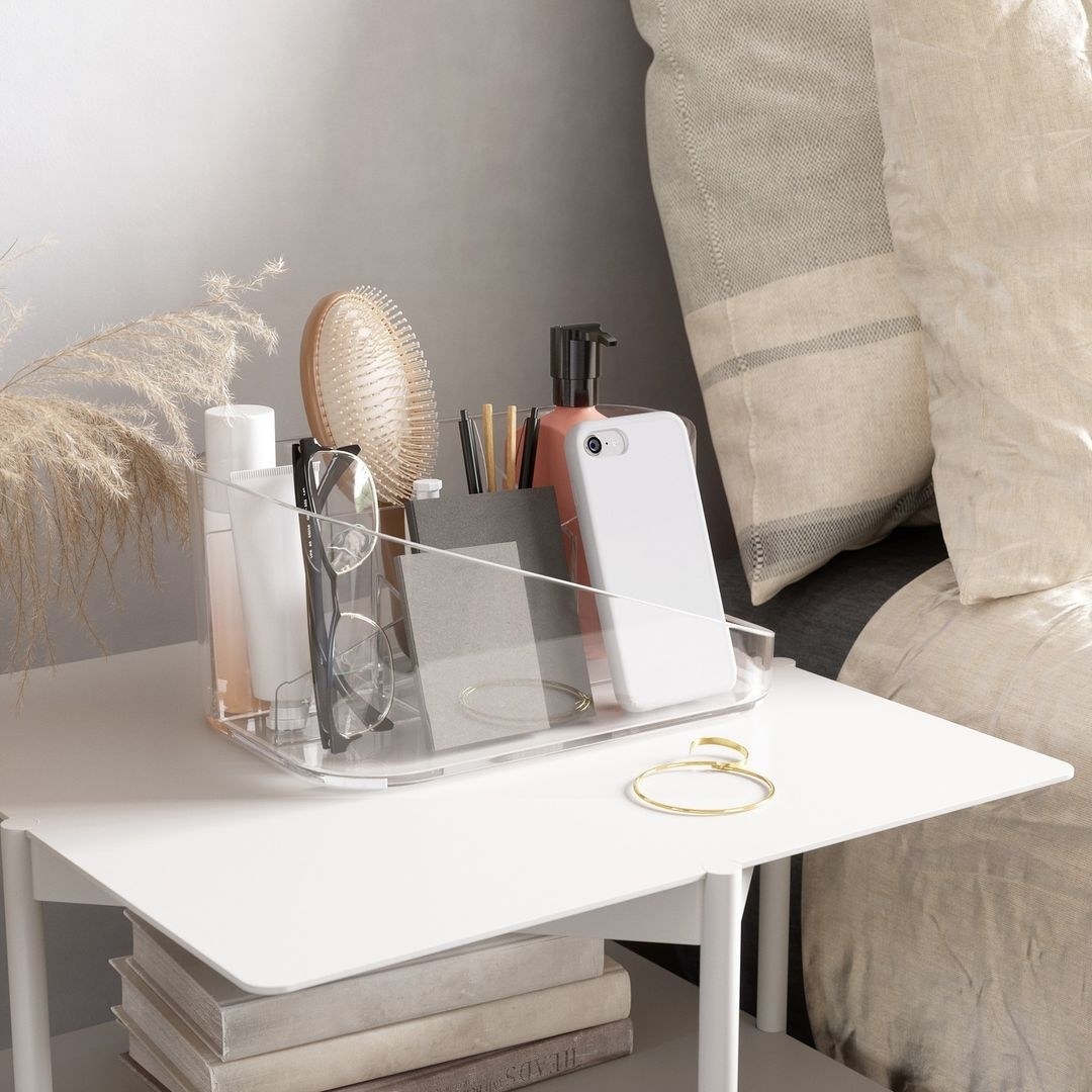 a transparent organizer on a nightstand filled with small accessories