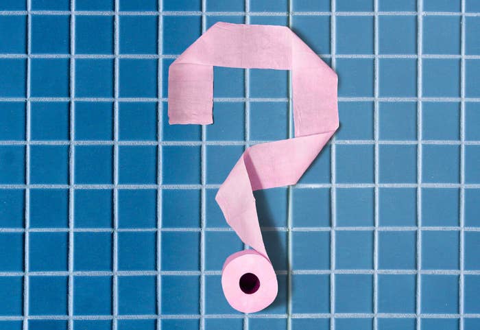 A roll of toilet paper rolled out on a blue tiled floor in the shape of a question mark.