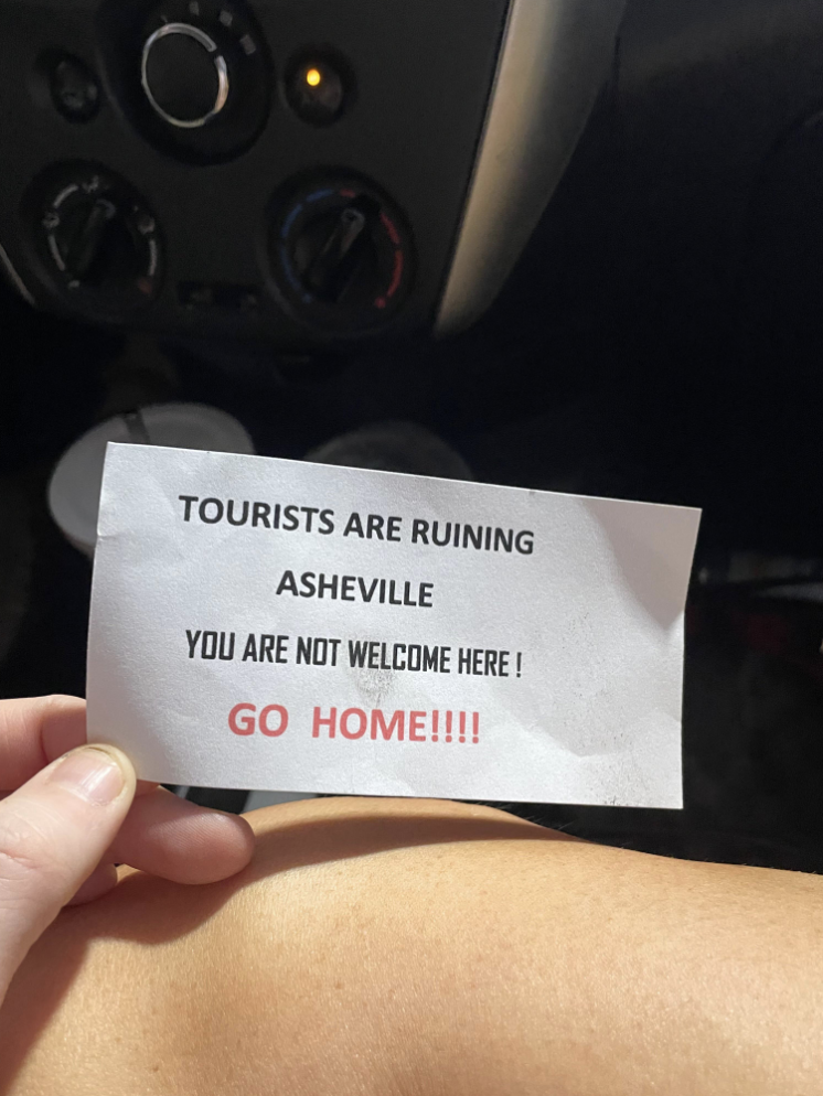 printed note that says tourists are ruining ashville