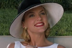 meredith, the stepmom from the '90s "parent trap," wears a red lip and wide-brimmed hat, smiling with all top teeth showing